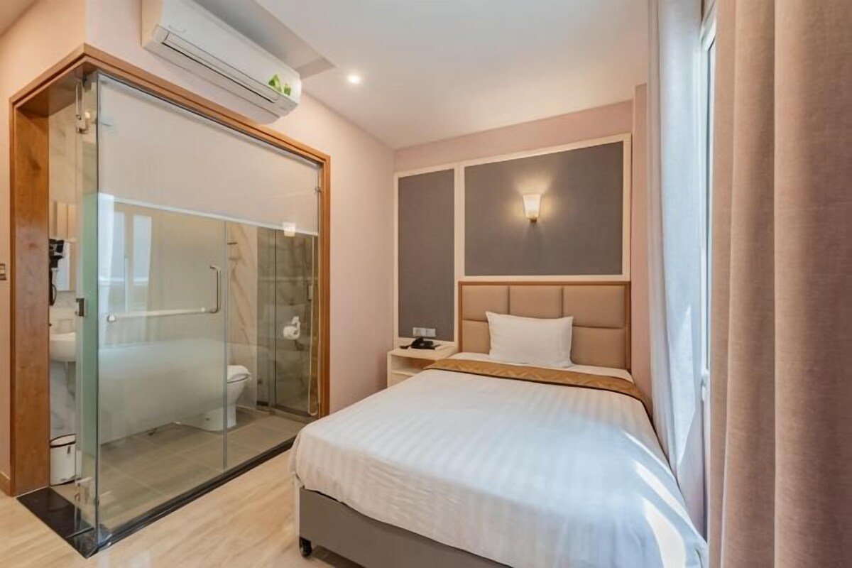 A hotel room with a glass-enclosed shower, a bed with a headboard, a bedside table, and a nightstand.