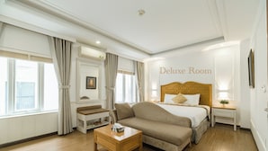 Ein Deluxe-Zimmer mit einem großen Bett, einem Holztischchen, einer Couch und einem Nachttisch mit Lampe.