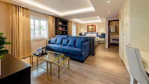 Ein modernes Hotelzimmer mit einem blauen Sofa, einem Glastisch, Holzböden und Blick auf die Stadt durch große Fenster.