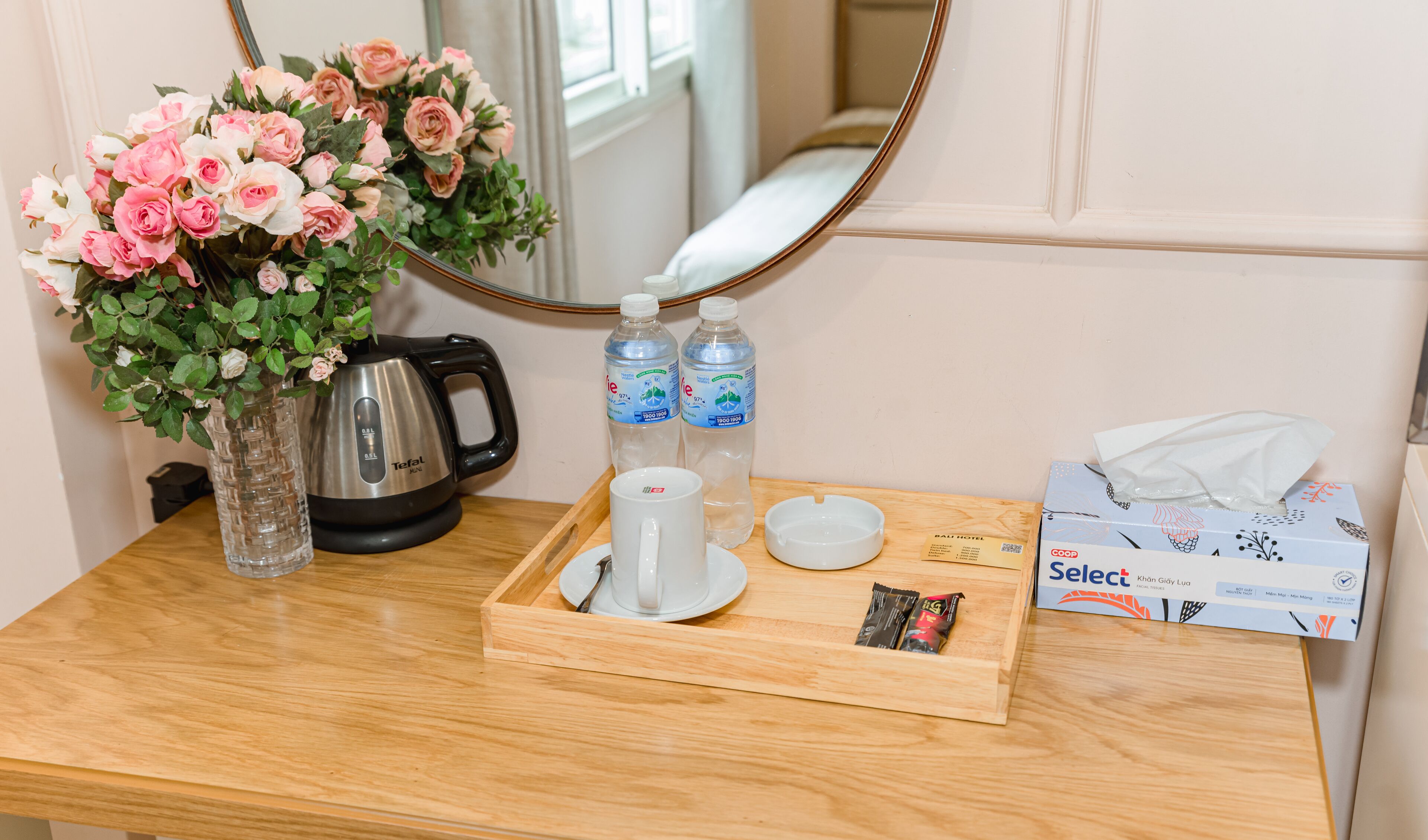 Dans une chambre d’hôtel, un plateau contenant une théière, des tasses, des bouteilles d’eau, une boîte de mouchoirs et un petit paquet de collations est préparé pour le petit-déjeuner.