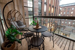 A balcony with a hanging chair, a round table with chairs, and a potted plant.