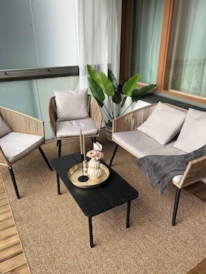 A balcony with wicker furniture, a black table, and a potted plant.