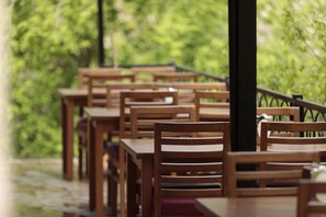 A row of wooden tables and chairs in an outdoor setting with a view of greenery. - Ahsen Pansiyon (Selçuk)
