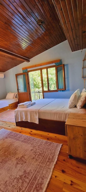 A cozy room with a wooden ceiling, a large bed with a wooden headboard, a small desk, and a window with curtains. - Ahsen Pansiyon (Selçuk)
