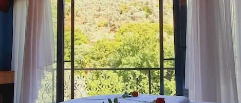 Un dormitorio con un ventanal grande, cortinas blancas y una cama con pétalos de rosa.