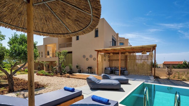Et poolområde med liggestole, en pergola og en bygning med moderne arkitektur.