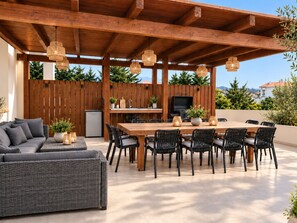 An outdoor patio with a wooden pergola, a dining table with chairs, a sofa, and a grill.
