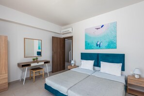 A bedroom with a bed, a desk, a chair, a mirror, and a painting of a beach scene.