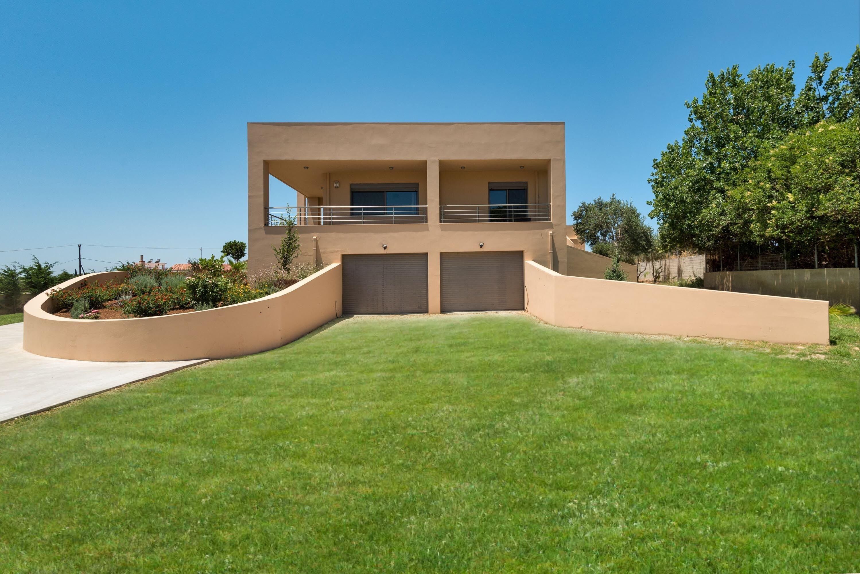 A modern two-story house with a curved driveway, a flat roof, and a large front lawn.