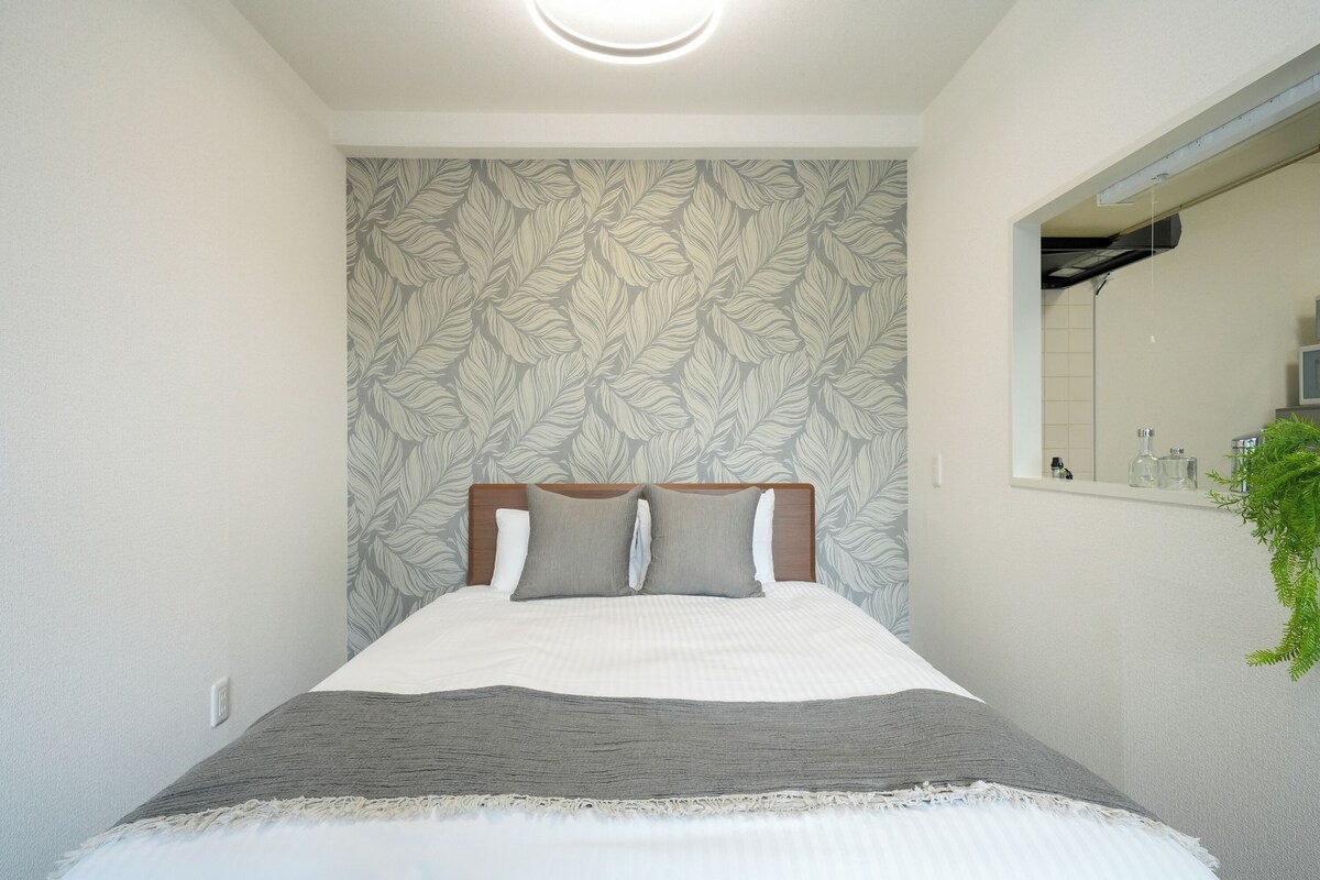 A neatly made bed with a headboard, a wall with a leaf pattern, and a mirror on the right.