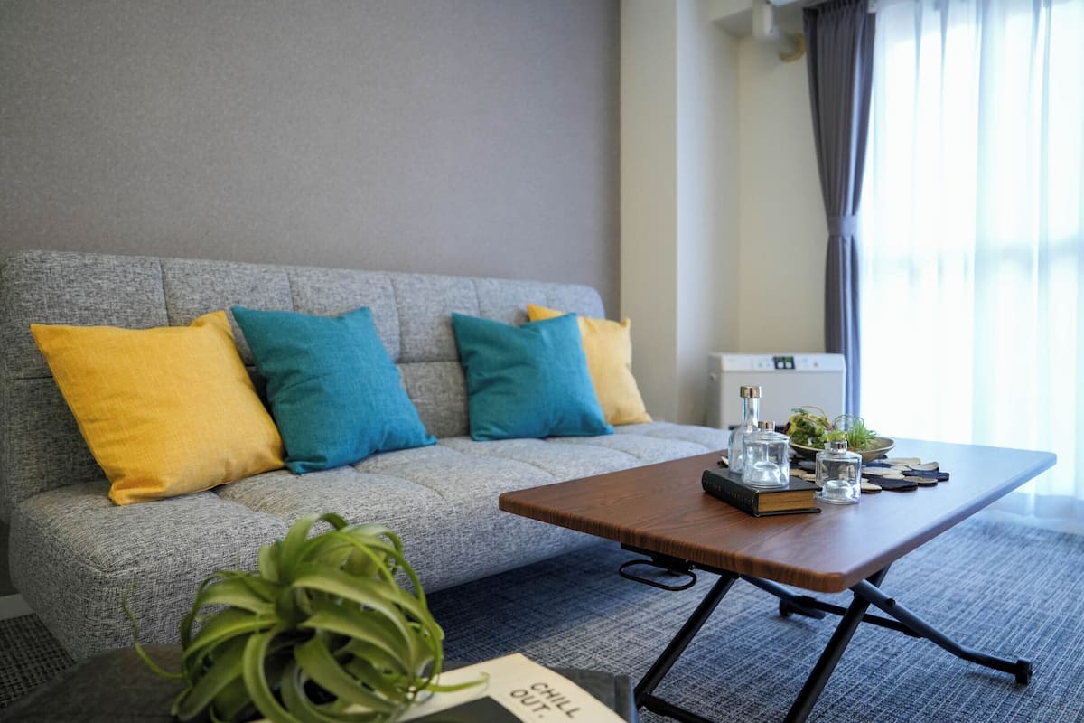 Una sala de estar moderna con un sofá gris, almohadones de colores, una mesa de centro de madera, una planta pequeña y un cartel que dice "CHILL OUT".
