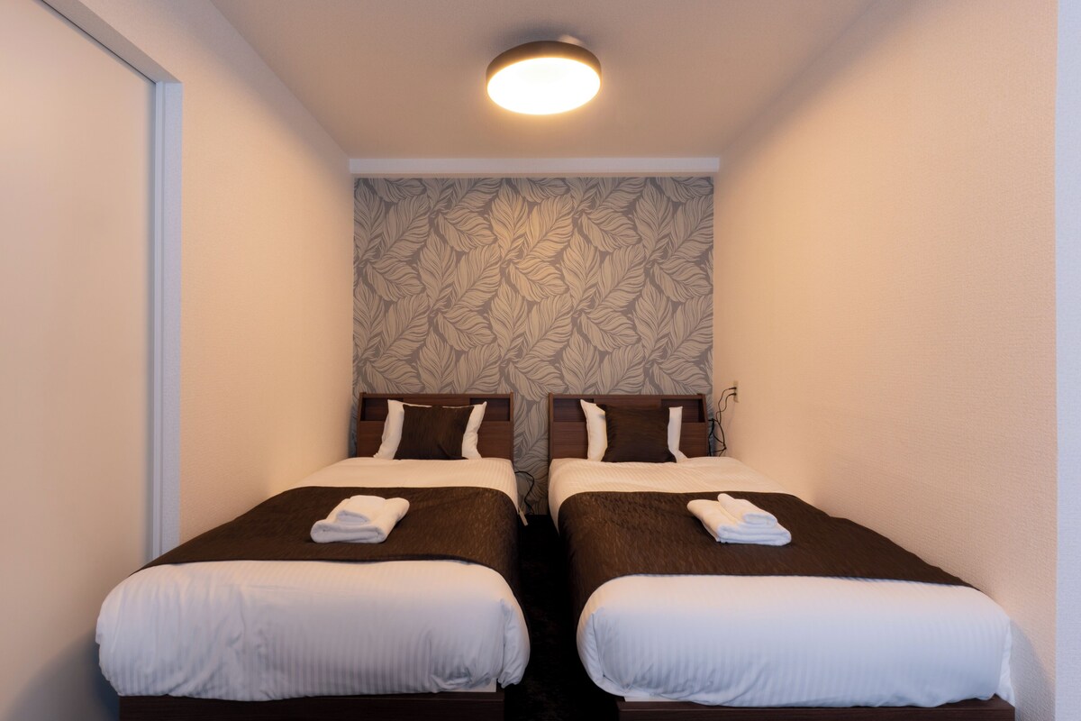 A hotel room with two single beds, a patterned wallpaper, and a ceiling light.