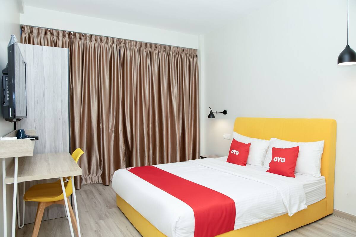 A hotel room with a bed, a desk, a chair, a television, and curtains.