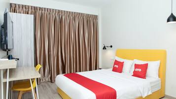 A hotel room with a bed, a desk, a chair, a television, and curtains.