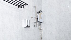 Une salle de bain avec des toilettes blanches, une douche équipée d’un pommeau de douche amovible et un porte-serviettes.