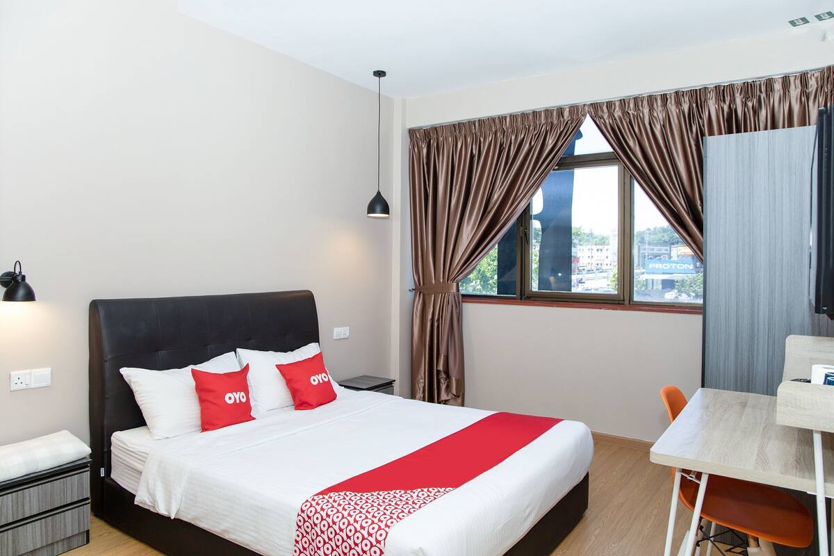 A hotel room with a bed, a desk, a chair, and a window with curtains.
