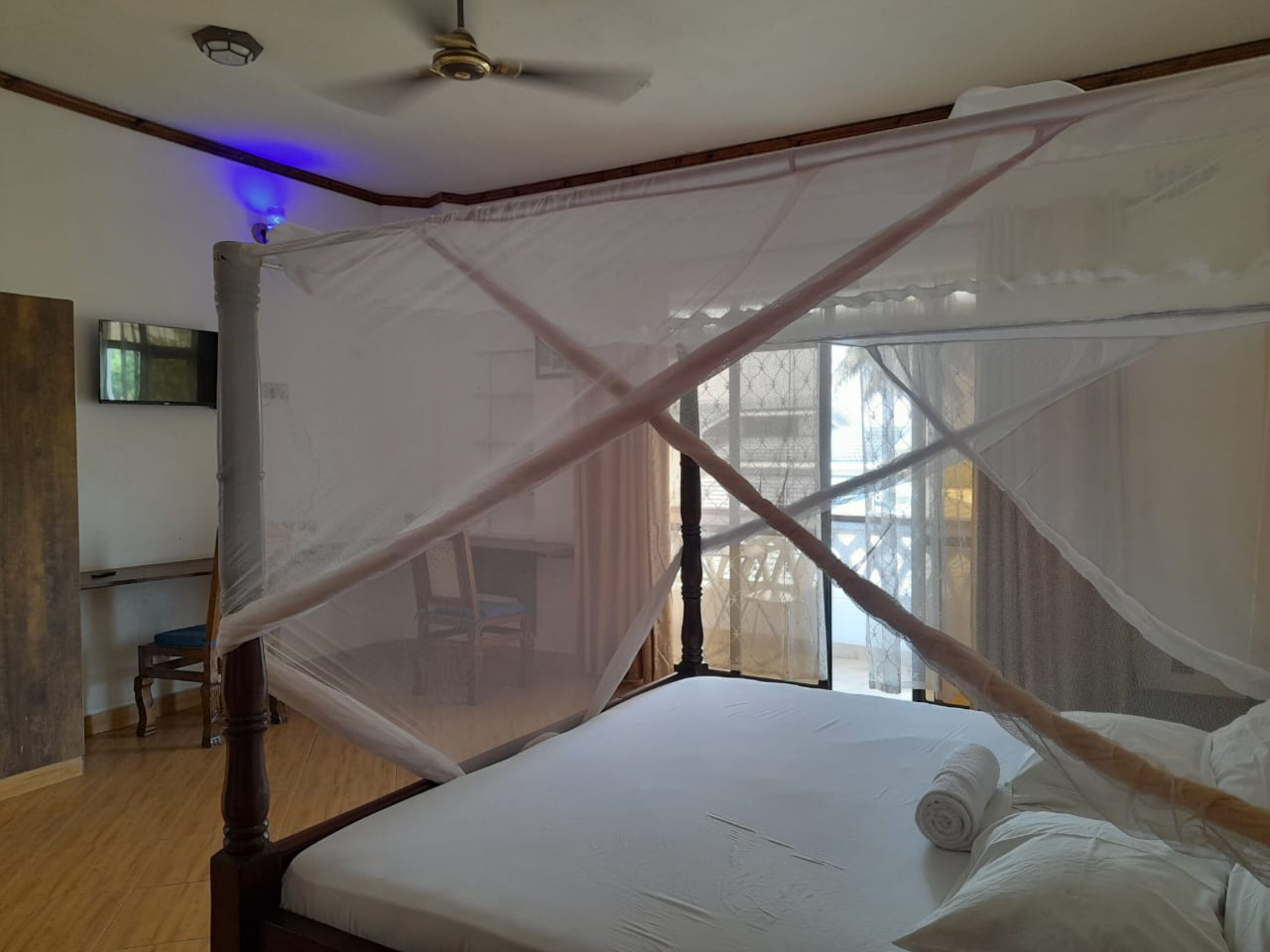 Un letto a baldacchino con zanzariera, pavimento in legno e ventilatore a soffitto.