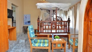 A room with a wooden bed, two chairs, a small table, and a TV. - Kilifi Blue House Resort (Kilifi)
