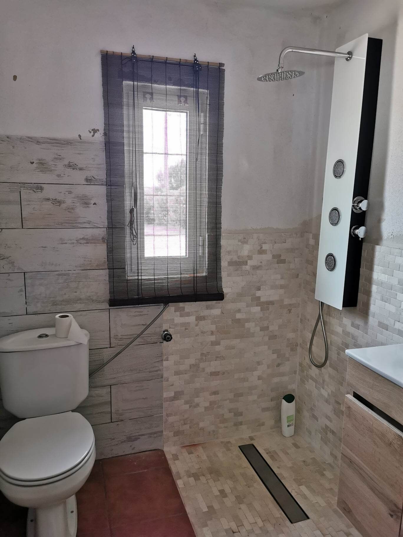 A bathroom with a toilet, a shower, and a window with blinds.