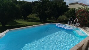 A rectangular swimming pool with clear blue water, surrounded by a wooden deck and a grassy area with trees. - Maison de Campagne au Calme (Ventosa)