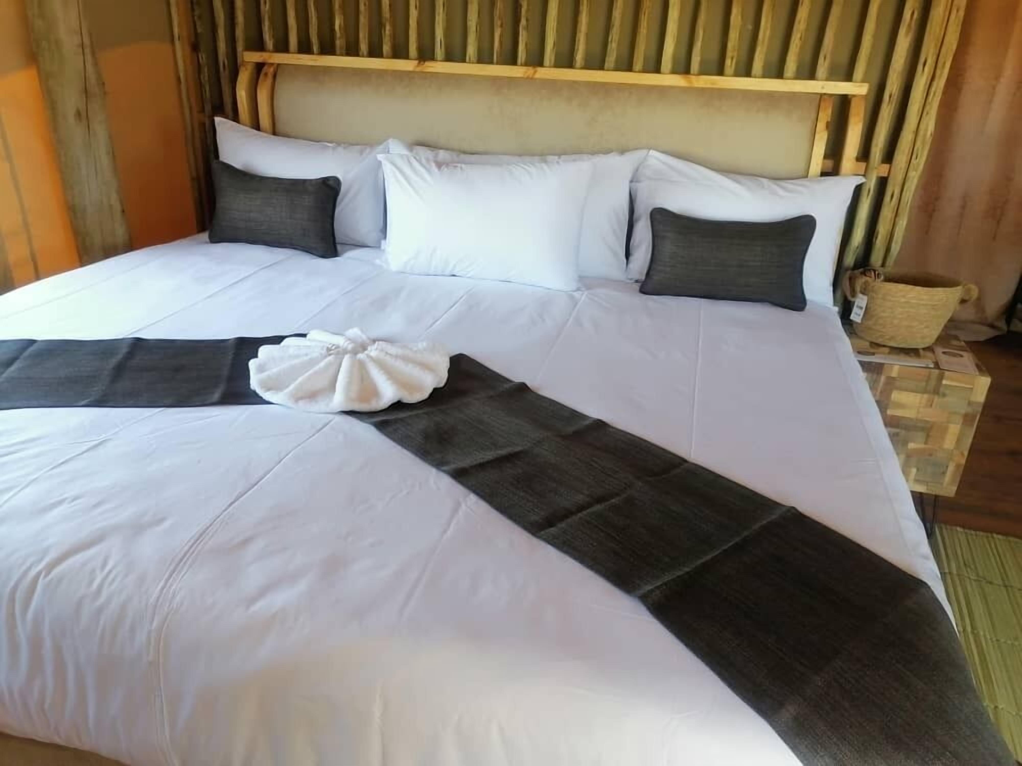 A large bed with white and dark bedding, a wooden headboard, and a woven basket on the floor.