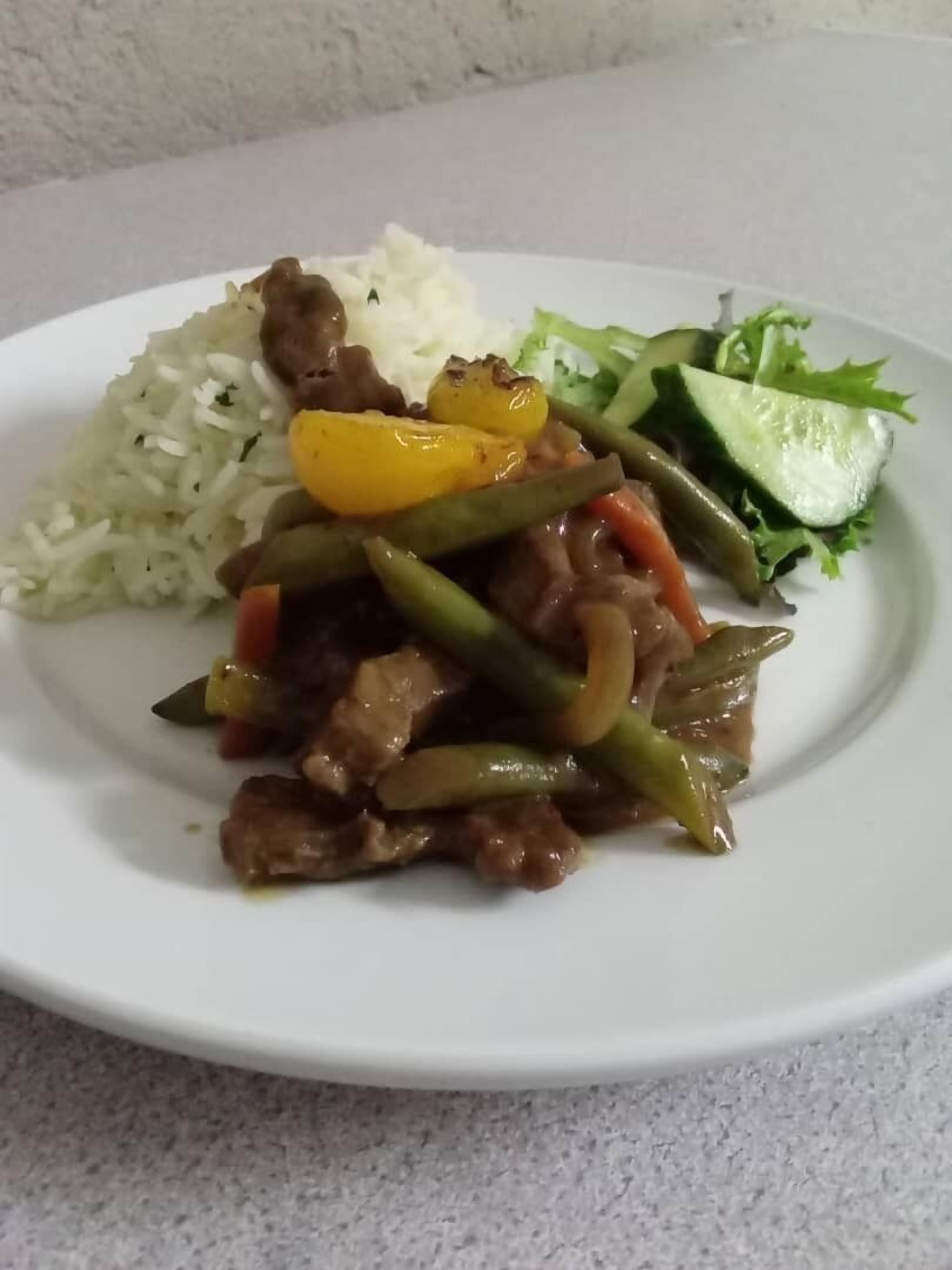 A plate of food with rice, beef, green beans, and a side salad.