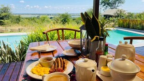 Une table à manger avec des aliments pour le petit-déjeuner, une vue sur une piscine et une végétation luxuriante.