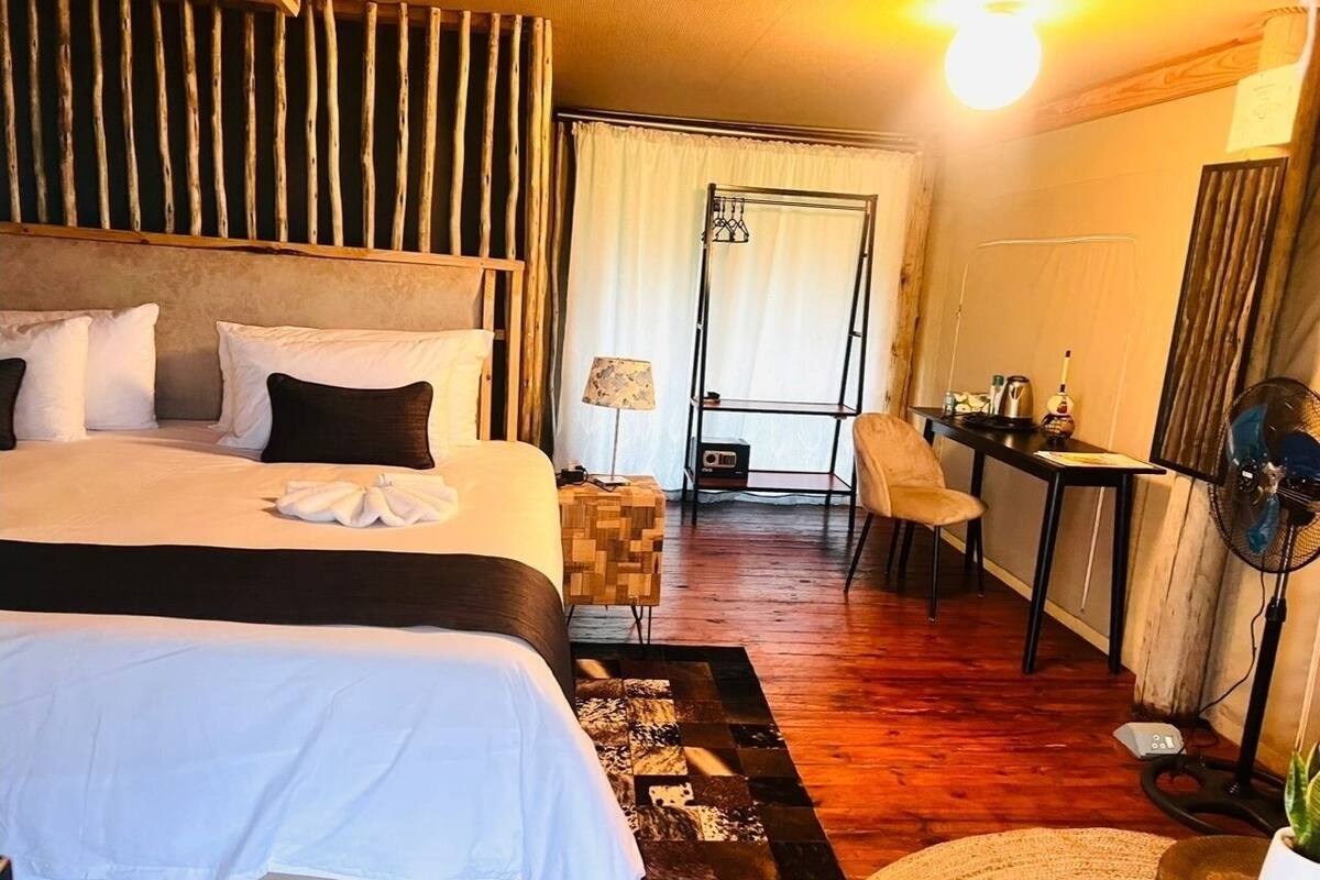 Une chambre d’hôtel avec un grand lit, un bureau, une chaise, un ventilateur et une fenêtre avec des rideaux.