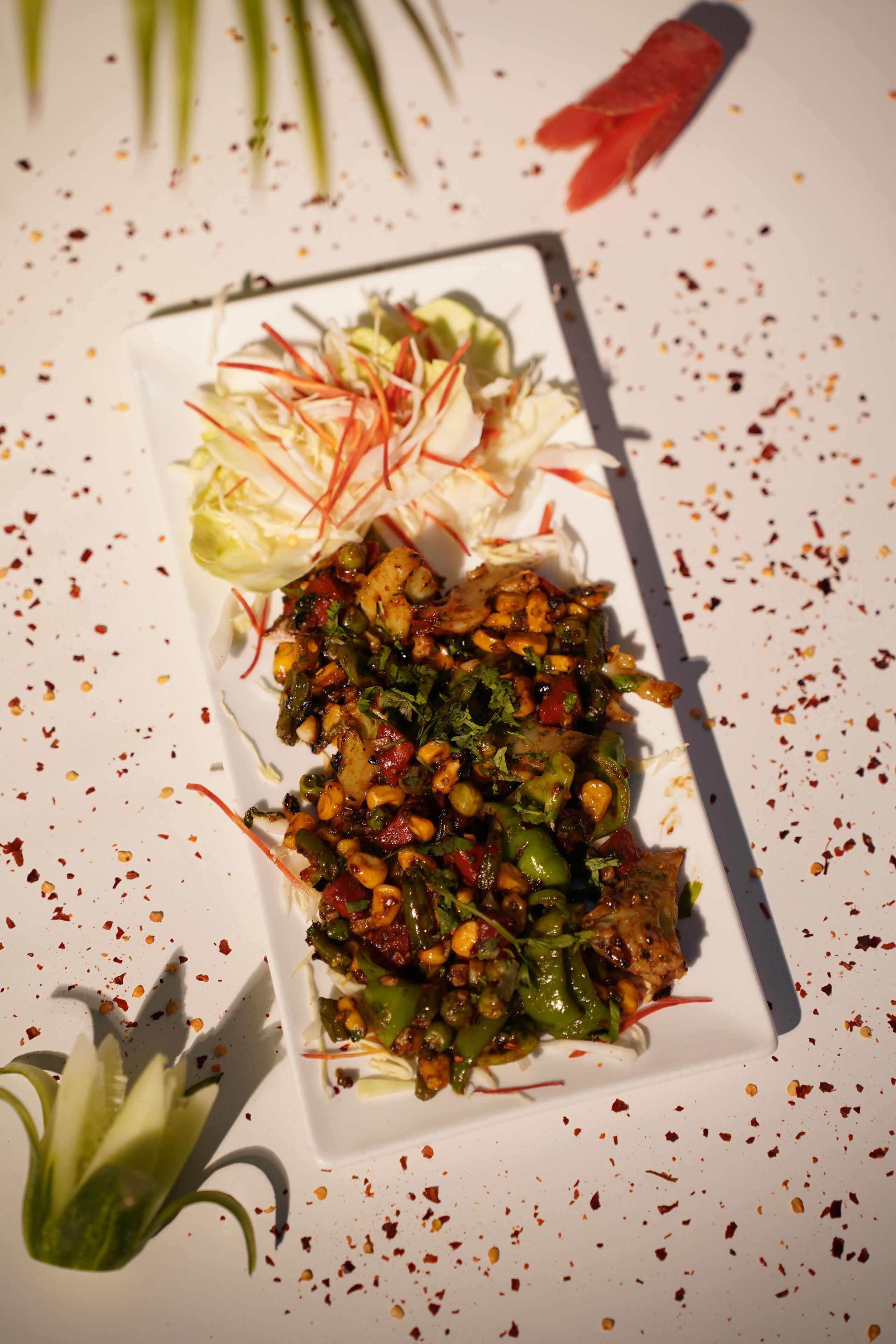A rectangular plate with a variety of food items, including a salad with shredded vegetables, a piece of meat, and a garnish of green leaves.