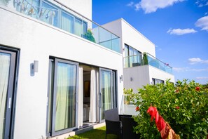 Un bâtiment moderne à deux étages, doté de grandes fenêtres en verre, d’un balcon agrémenté de plantes et d’un jardin bien entretenu.