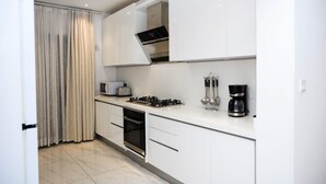 Una cocina moderna con muebles blancos, estufa a gas, microondas y cafetera.