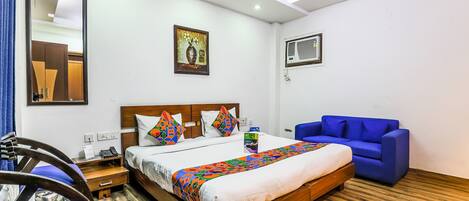 A hotel room with a bed, a blue sofa, a wooden nightstand, and a mirror.