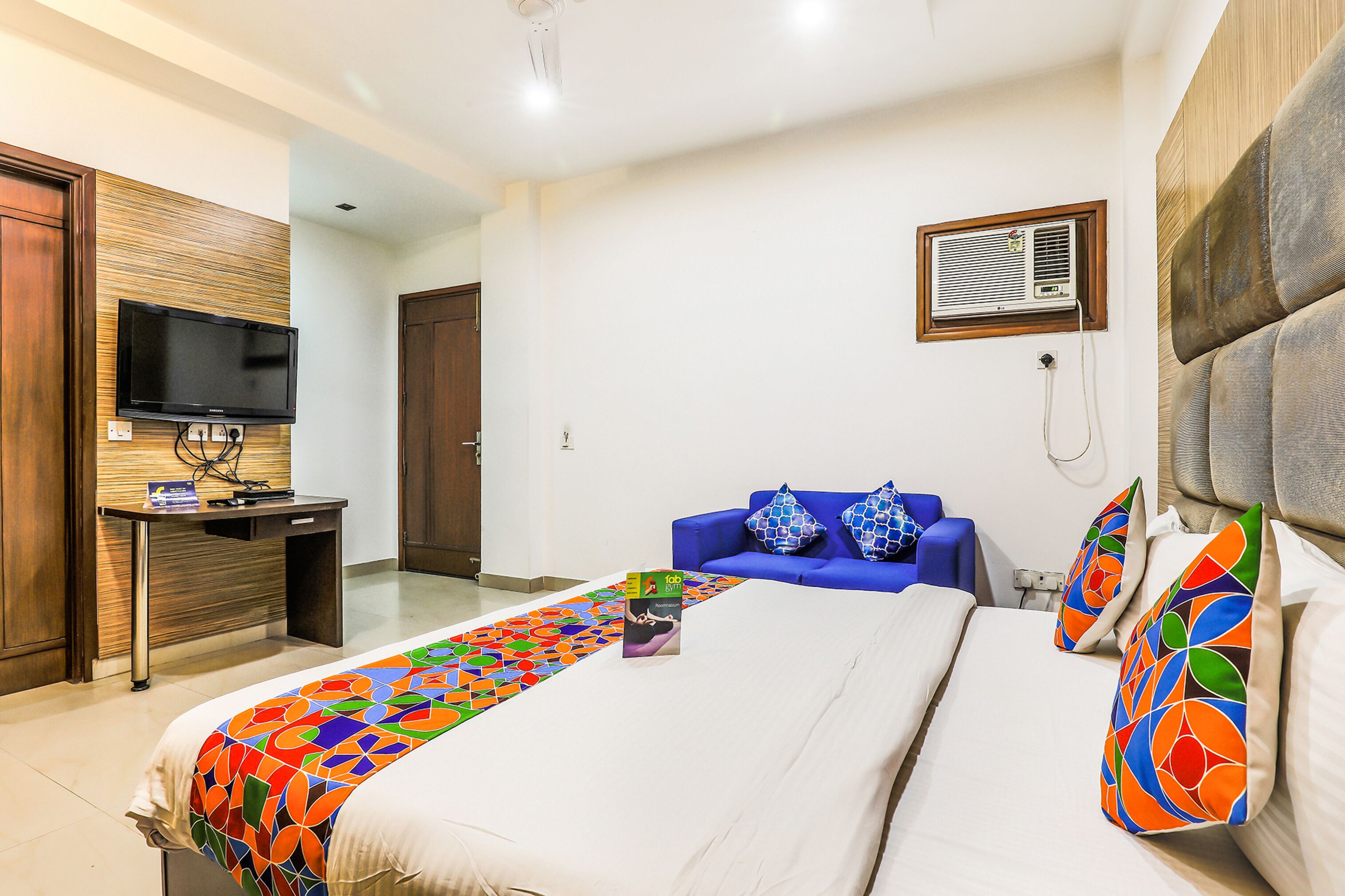 A hotel room with a bed, a desk, a television, and a blue sofa.
