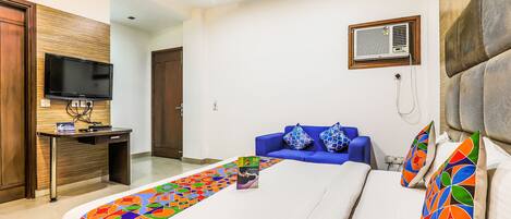 A hotel room with a bed, a desk, a television, and a blue sofa.