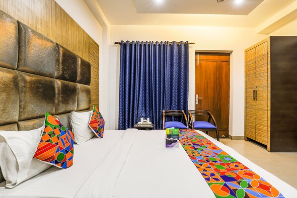 Una habitación de hotel con una cama grande, un cabecero de madera, una cortina azul, un armario de madera y una mesita con una silla.