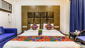 A hotel room with a large bed, a blue sofa, a wooden headboard, and a patterned curtain. - FabHotel The Maple Stays - Nr. Leisure Valley Park, Iffco Chowk (Gurugram)