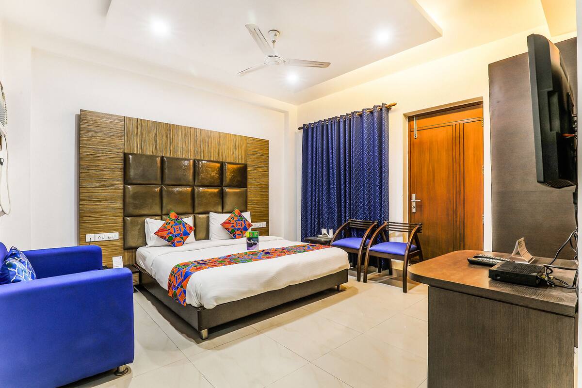 Una habitación de hotel con cama, escritorio, silla, televisión y ventilador de techo.