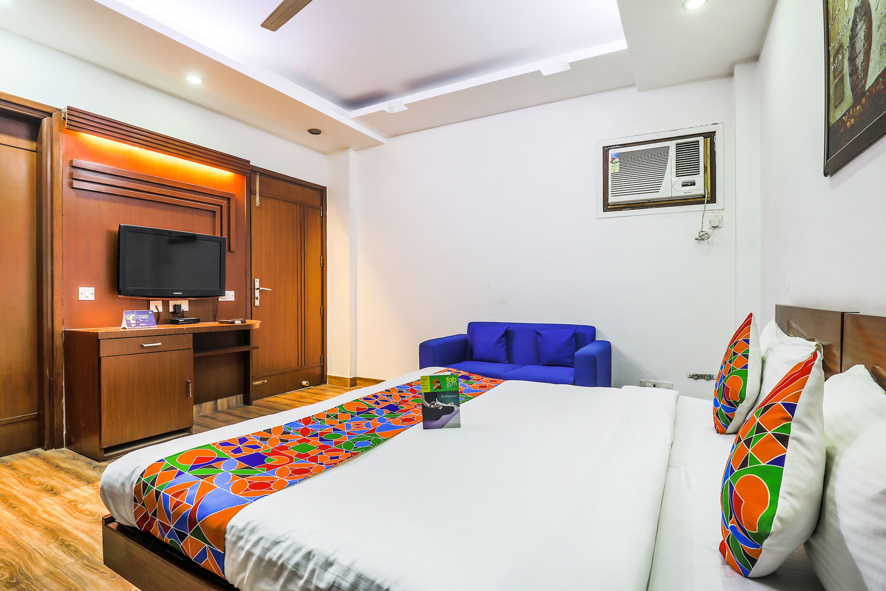 Une chambre d’hôtel avec un lit, une télévision, un bureau, un canapé bleu et un ventilateur de plafond.
