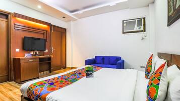 A hotel room with a bed, a TV, a desk, a blue sofa, and a ceiling fan.