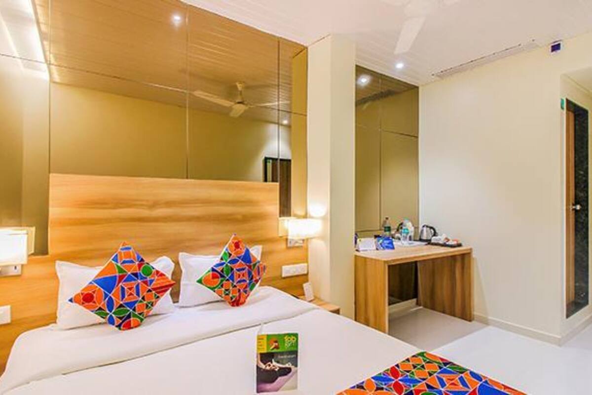 Quarto de hotel moderno com cabeceira de madeira, mesa de cabeceira com abajur, escrivaninha pequena e espelho.