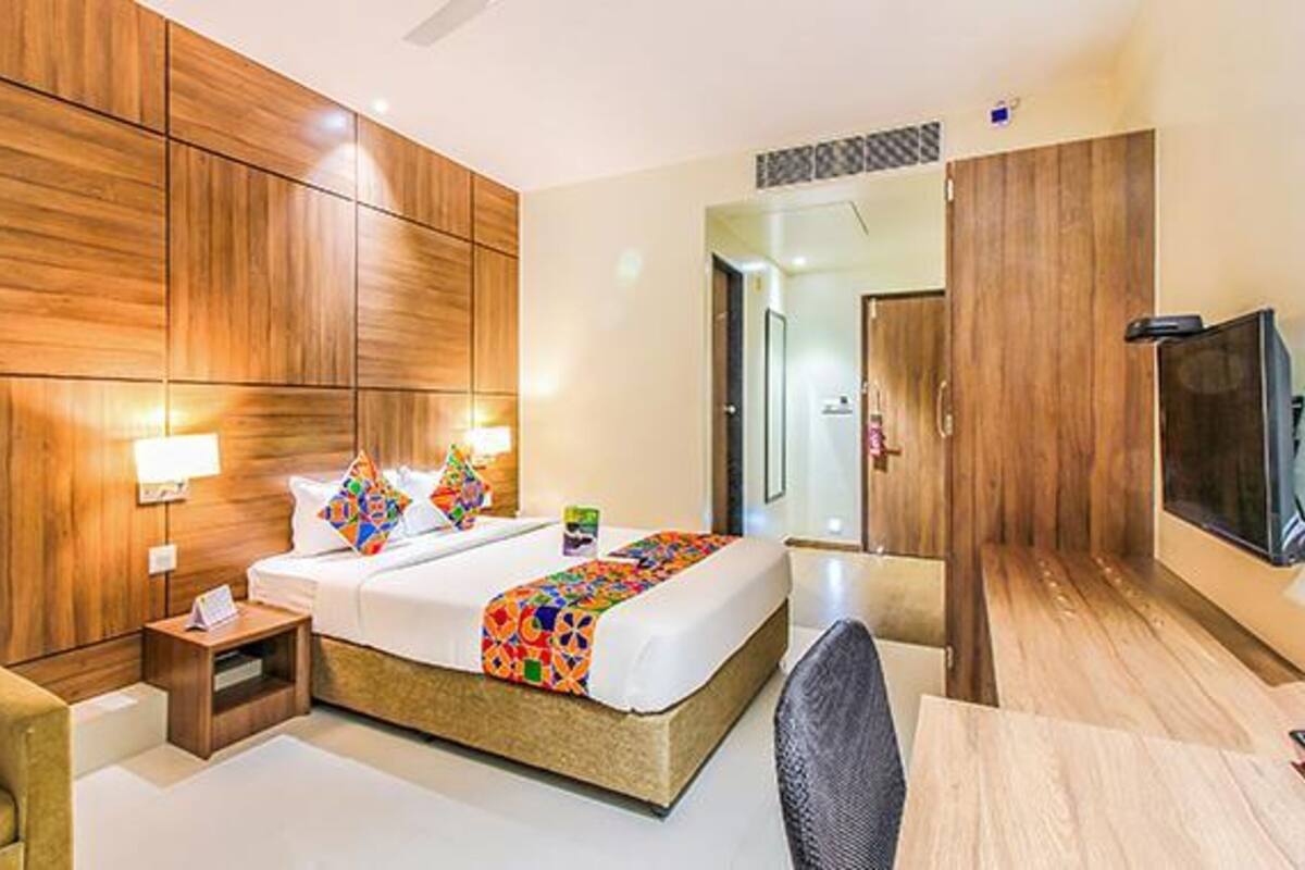 Quarto de hotel com uma cama grande, paredes de painel de madeira, uma TV e uma pequena escrivaninha.