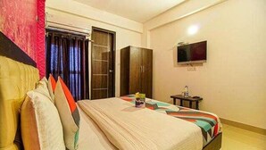 A bedroom with a bed, a wardrobe, a television on the wall, and a small table with a bottle. - FabHotel TP Suites (New Delhi)