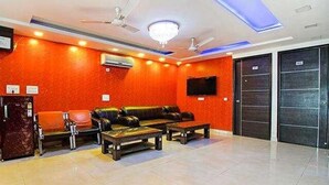 A lobby with a red wall, leather sofas, a coffee table, a ceiling fan, and a TV mounted on the wall. - FabHotel TP Suites (New Delhi)