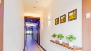 A hotel hallway with a wooden floor, a wooden bench with potted plants, and framed pictures on the wall. - FabHotel Devanshi Inn (Panvel)