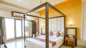 A four-poster bed with a colorful bedspread, a bedside table with a remote control, and a wall-mounted lamp. - FabHotel Devanshi Inn (Panvel)