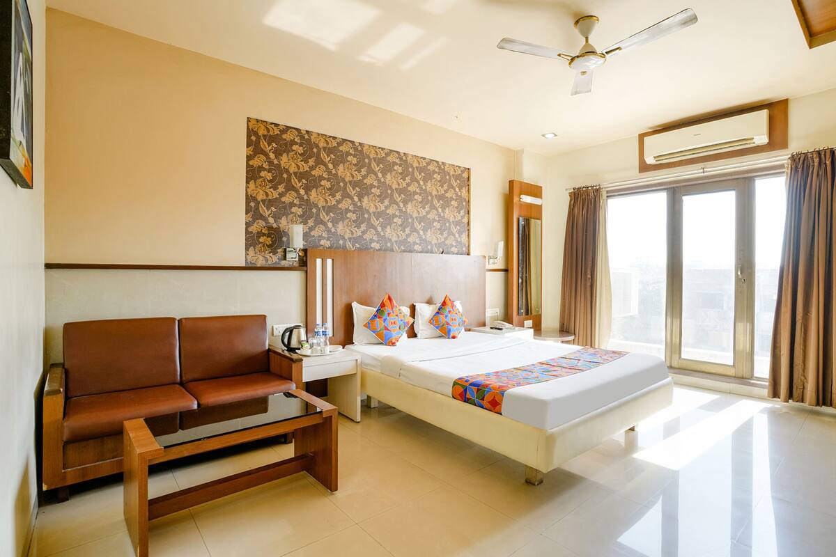 A hotel room with a bed, a sofa, a desk, and a ceiling fan.