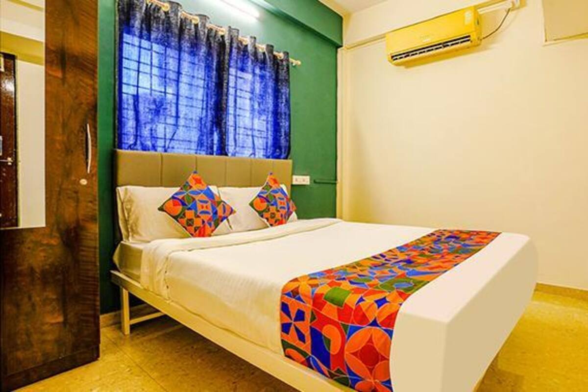 A bed with colorful pillows, a white headboard, and a blue curtain.