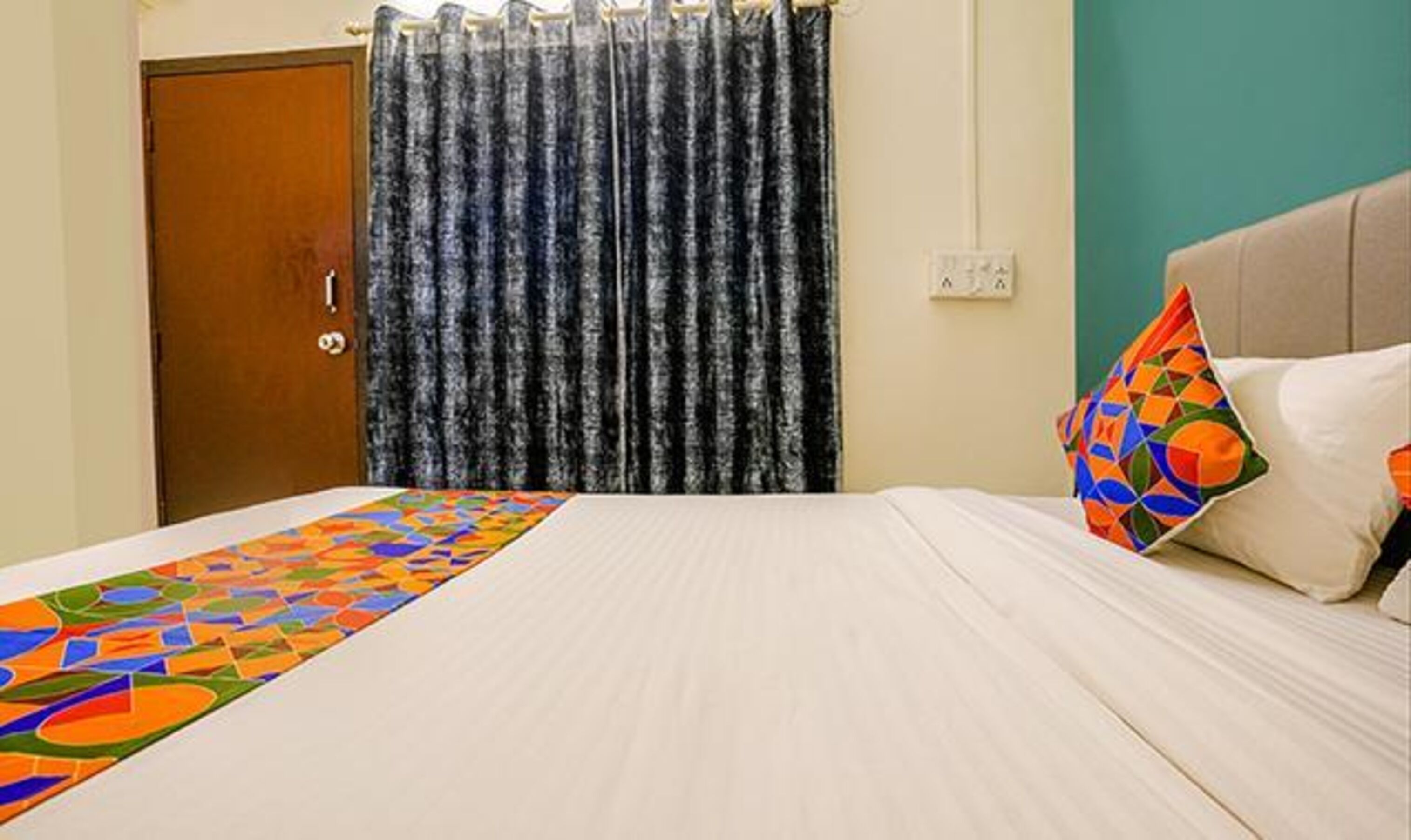 A hotel room with a bed, a curtain, a pillow, and a wall socket.