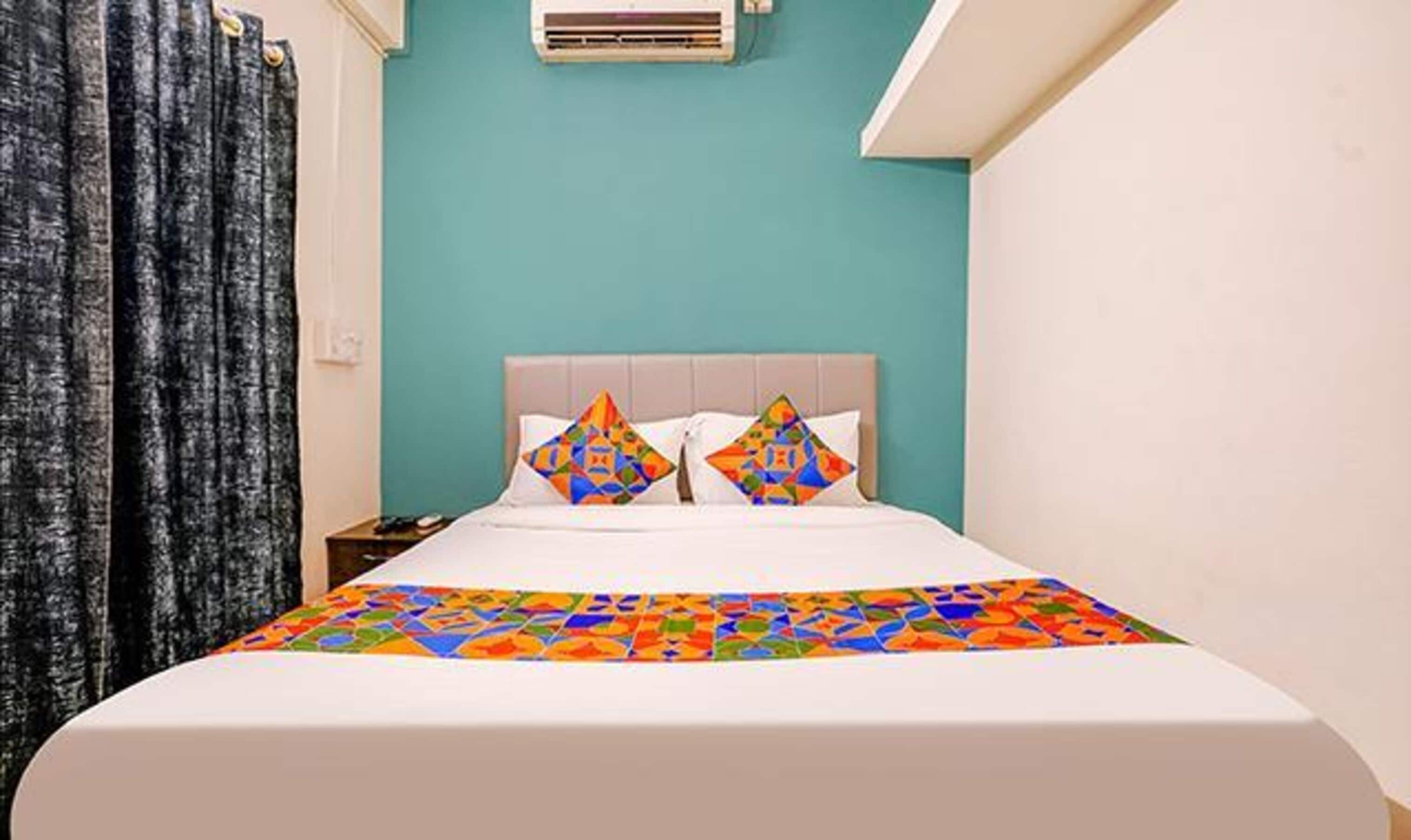 A hotel room with a bed, a nightstand, a wall-mounted air conditioner, and a window with curtains.