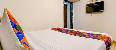 A single bed with a colorful quilt and a white pillow in a room with a flat-screen TV mounted on the wall.